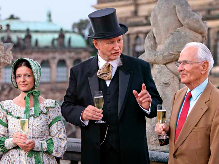 На фоне Дворца Цвингер в Дрездене: Вальтер Ланге (справа) беседует с двумя актерами, выступающими в роли прадеда-основателя Фердинанда А. Ланге и его жены Антонии.